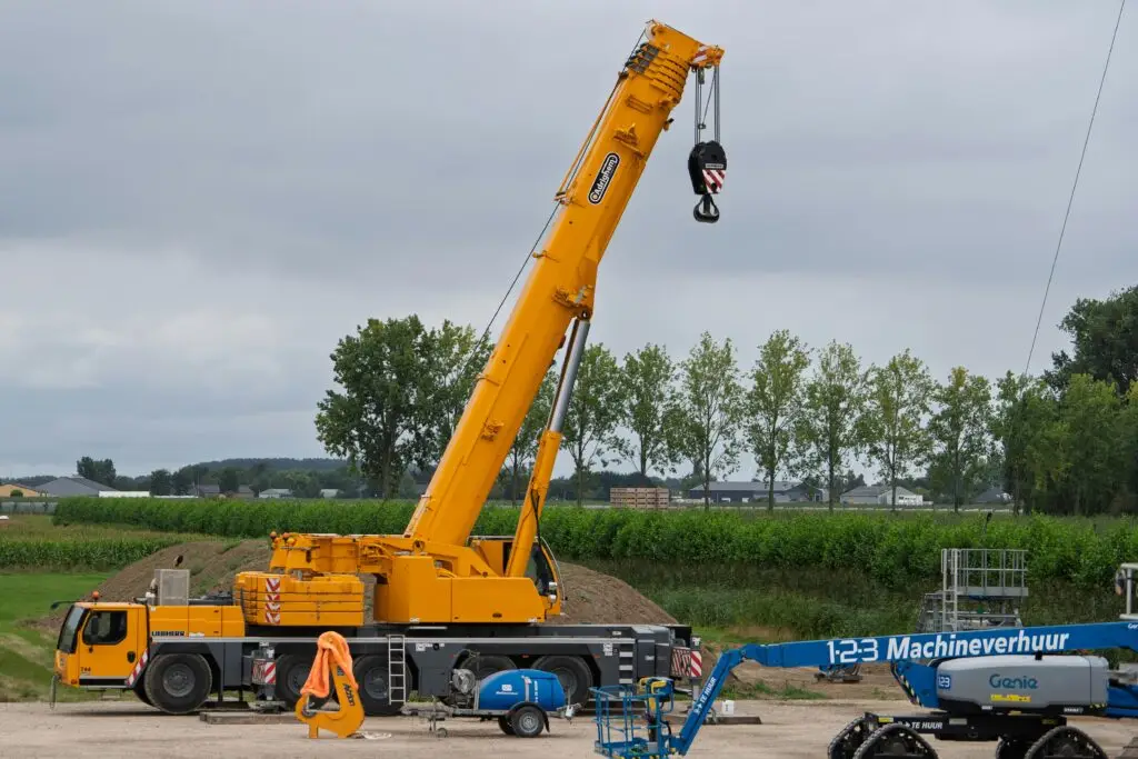 A large yellow crane at a construction site with lush greenery in the background.